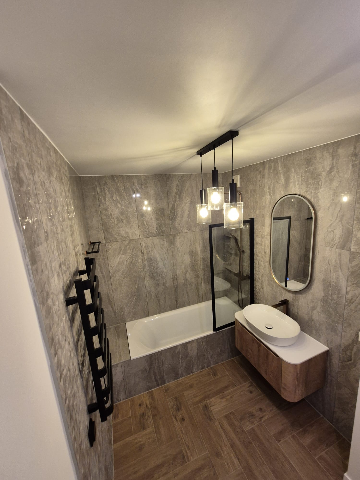 Badkamer met visgraatvloer, ligbad en zwarte radiator